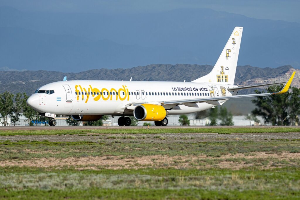 Flybondi airplane on runway with mountains in background. Captured in clear daylight.