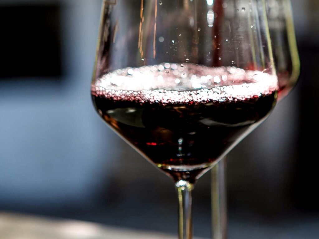 Close-up of red wine being poured into a glass, showcasing rich color and bubbles.